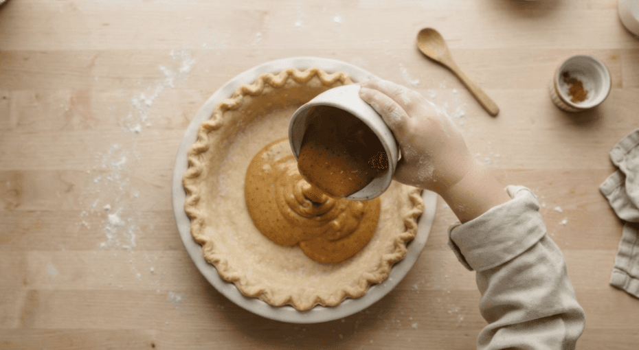 A child pouring pumpkin pie filling into a crust